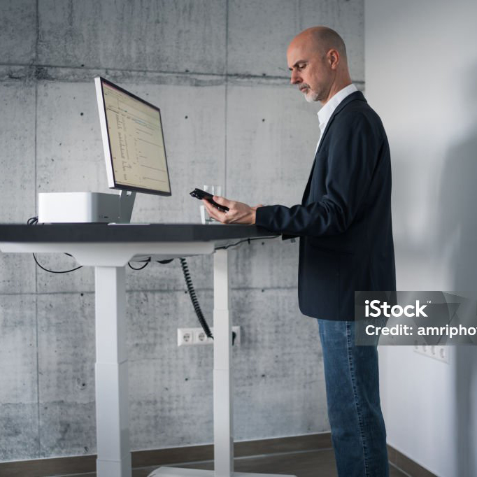 Mann steht am ergonomischen Tisch und arbeitet am PC